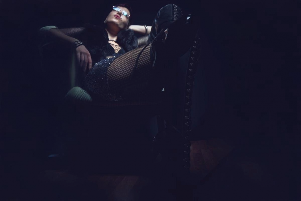Dunkel/farbig, Sessel im Hintergrund, Latex-Overknees, Netzstrümpfe, Pailletten-Hotpants, Blick nach oben ins Licht
